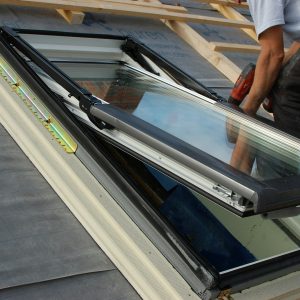 Assembling / fitting a roof window / skylight with reflection of worker in window glass